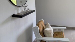 Una habitación moderna con un espejo redondo, un estante pequeño con vasos, una mecedora blanca y adornos hexagonales en la pared.