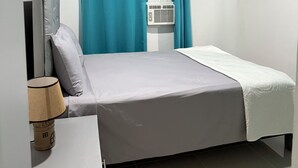 Un dormitorio con cama, cortinas, ventana, lámpara de noche y un calefactor.