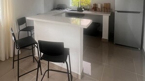 Una cocina moderna con una isla central, taburetes negros tipo barra, un refrigerador y una ventana con follaje exterior.