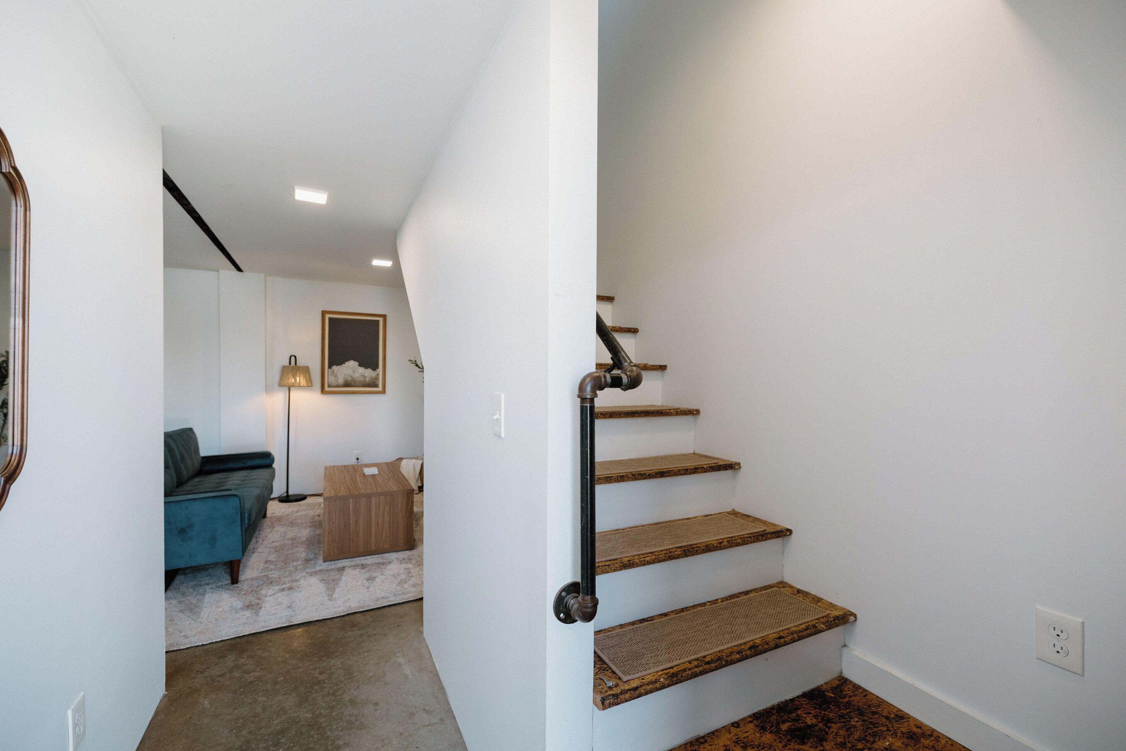 A staircase with wooden steps and a metal handrail, leading to a landing with a sofa and a lamp.