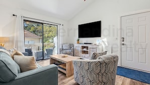 A modern living room with a sofa, armchair, and coffee table. There is a TV mounted on the wall and a sliding glass door leading to an outdoor area. - Experience tranquility at 2585 Forest Ridge-Cranes Landing, charming 2-BR retreat, Fernandina Beach (Fernandina Beach)