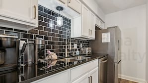 A modern kitchen with white cabinets, black backsplash, stainless steel appliances, and a built-in dishwasher. - Experience tranquility at 2585 Forest Ridge-Cranes Landing, charming 2-BR retreat, Fernandina Beach (Fernandina Beach)