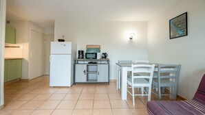 A compact kitchen with a refrigerator, microwave, coffee maker, and a small cabinet. There is a dining table with chairs and a single bed in the corner. - Apartment, terrace, beach within walking distance (Agde)