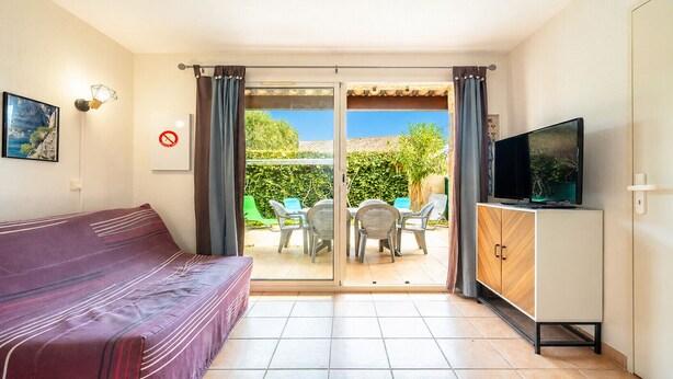 A room with a sofa, a TV on a cabinet, a sliding glass door to an outdoor area with chairs and a table. - Apartment, terrace, beach within walking distance (Agde)