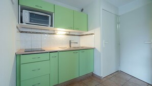 A compact kitchen with green cabinets, a microwave, and a tiled backsplash. - Apartment, terrace, beach within walking distance (Agde)