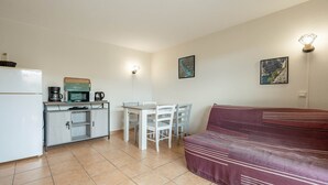 A compact living space with a kitchenette, a dining table with chairs, a sofa, and two wall-mounted light fixtures. - Apartment, terrace, beach within walking distance (Agde)