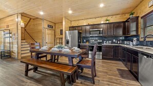 Une cuisine moderne avec des meubles de couleur bois foncé, des appareils en acier inoxydable et une table à manger en bois pouvant accueillir six personnes.