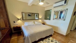 A bedroom with a bed, nightstands, wall-mounted mirrors, a ceiling fan, and a patterned rug. - Casa Corazon Unit 702 - Ocean View, huge terrace in beautiful Puerto Vallarta! (Puerto Vallarta)