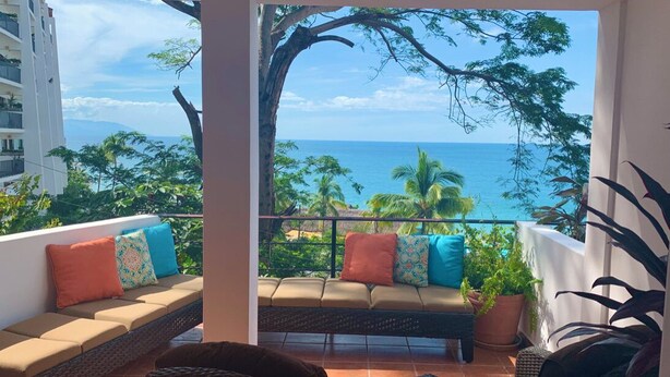 A balcony with a sofa and chairs, overlooking a coastal view with palm trees and the ocean. - Casa Corazon Unit 702 - Ocean View, huge terrace in beautiful Puerto Vallarta! (Puerto Vallarta)