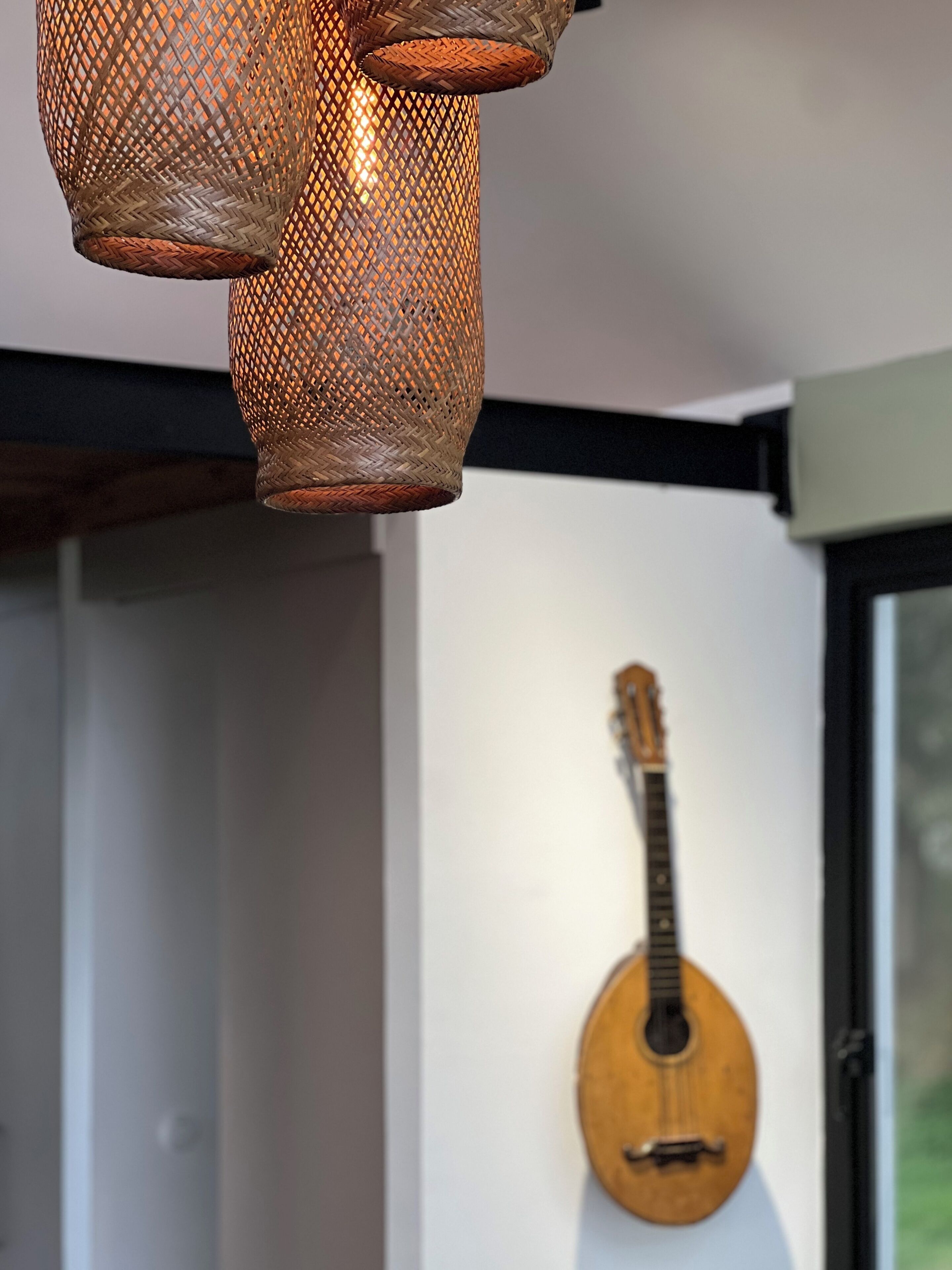 Een kamer met een geweven hanglamp en een gitaar aan de muur.