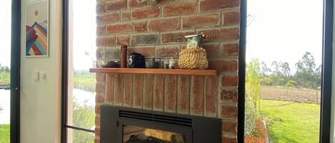 A modern living room with a brick fireplace, a mounted deer head, and a view of a green landscape through large windows.