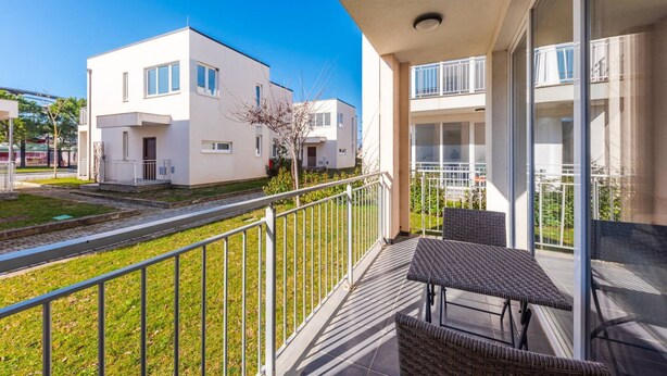 A balcony with wicker furniture, a clear view of a modern building, and a metal railing.