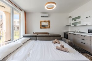 A modern hotel room with a large bed, a small sofa, a kitchen area, and a balcony with a view. - Blue Haven Talea Beachfront With Pool Access (Shënkoll)
