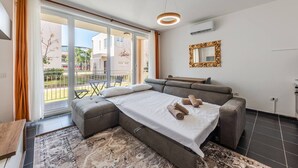 A modern bedroom with a large bed, a sofa, a dining table, and a view of the outside.