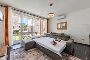 A modern bedroom with a large bed, a sofa, a dining table, and a view of the outside. - Blue Haven Talea Beachfront With Pool Access (Shënkoll)
