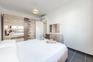 A modern bedroom with a large bed, wooden headboard, and a mirror above the dresser. - Blue Haven Talea Beachfront With Pool Access (Shënkoll)