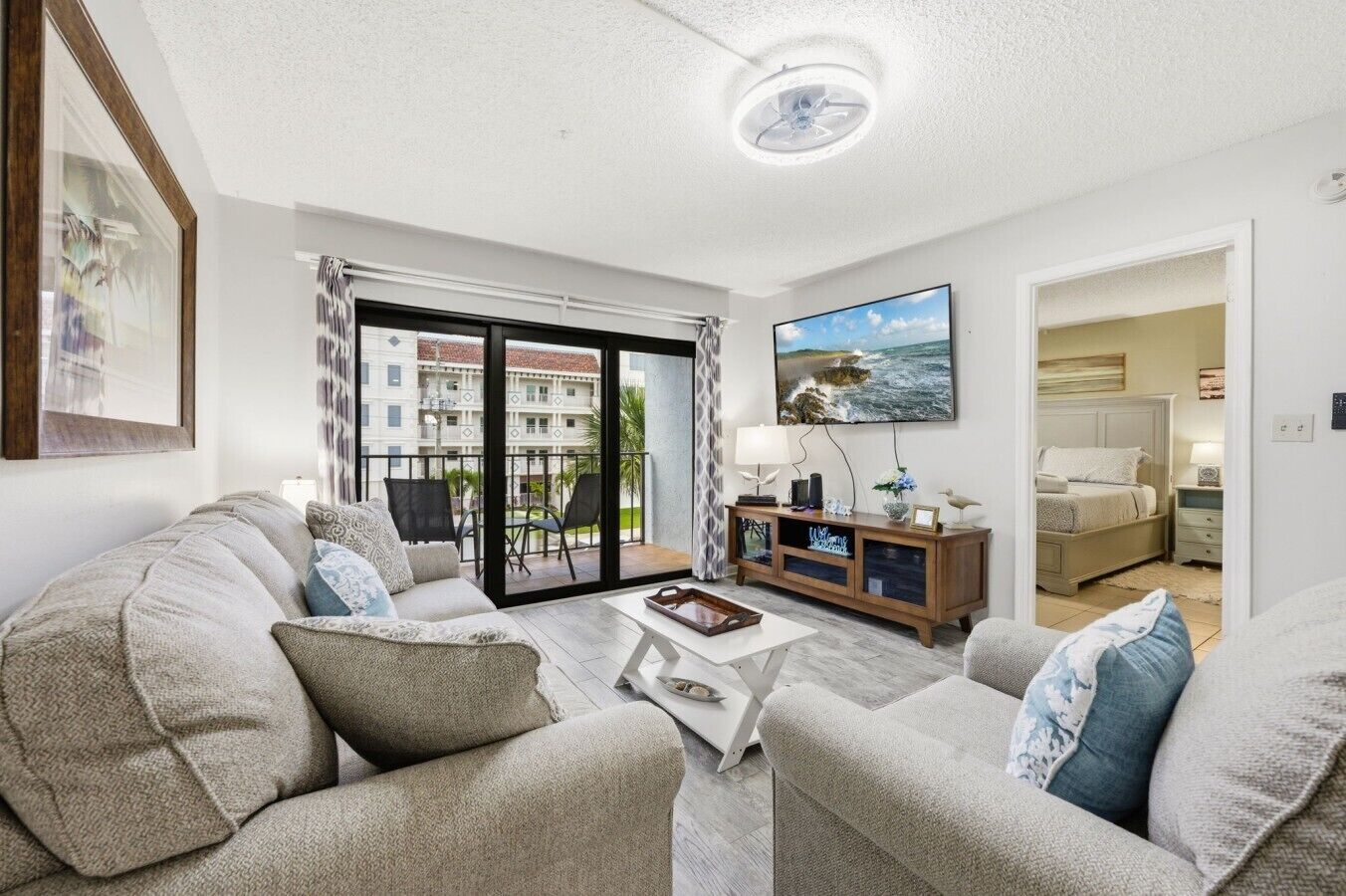A living room with a sofa, coffee table, TV, and a balcony with a view of buildings.