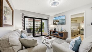 A living room with a sofa, coffee table, TV, and a balcony with a view of buildings.