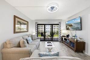 A living room with a sofa, a coffee table, a TV, and a balcony with a view of buildings.