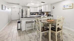 A modern kitchen with white cabinetry, a central island, and a dining area with wooden chairs.