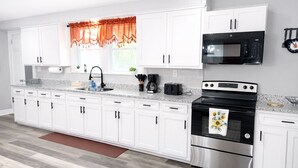 Una cocina moderna con armarios blancos, horno de acero inoxidable, microondas y cafetera.