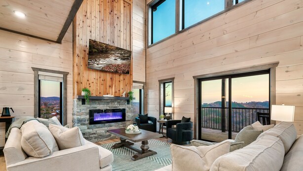A spacious living room with a stone fireplace, comfortable seating, and a large window overlooking a scenic view.
