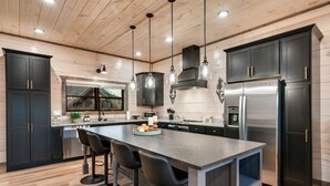 A modern kitchen with dark cabinets, stainless steel appliances, and a central island with bar stools.