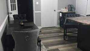 Uma cozinha compacta com área de jantar, destacando uma mesa de madeira escura, um banquinho e uma cafeteira.