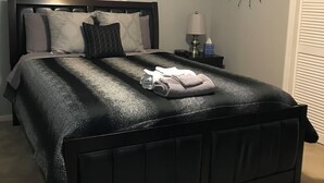 Quarto com cama preta, persianas brancas, luminária na parede e decoração em formato de estrela.