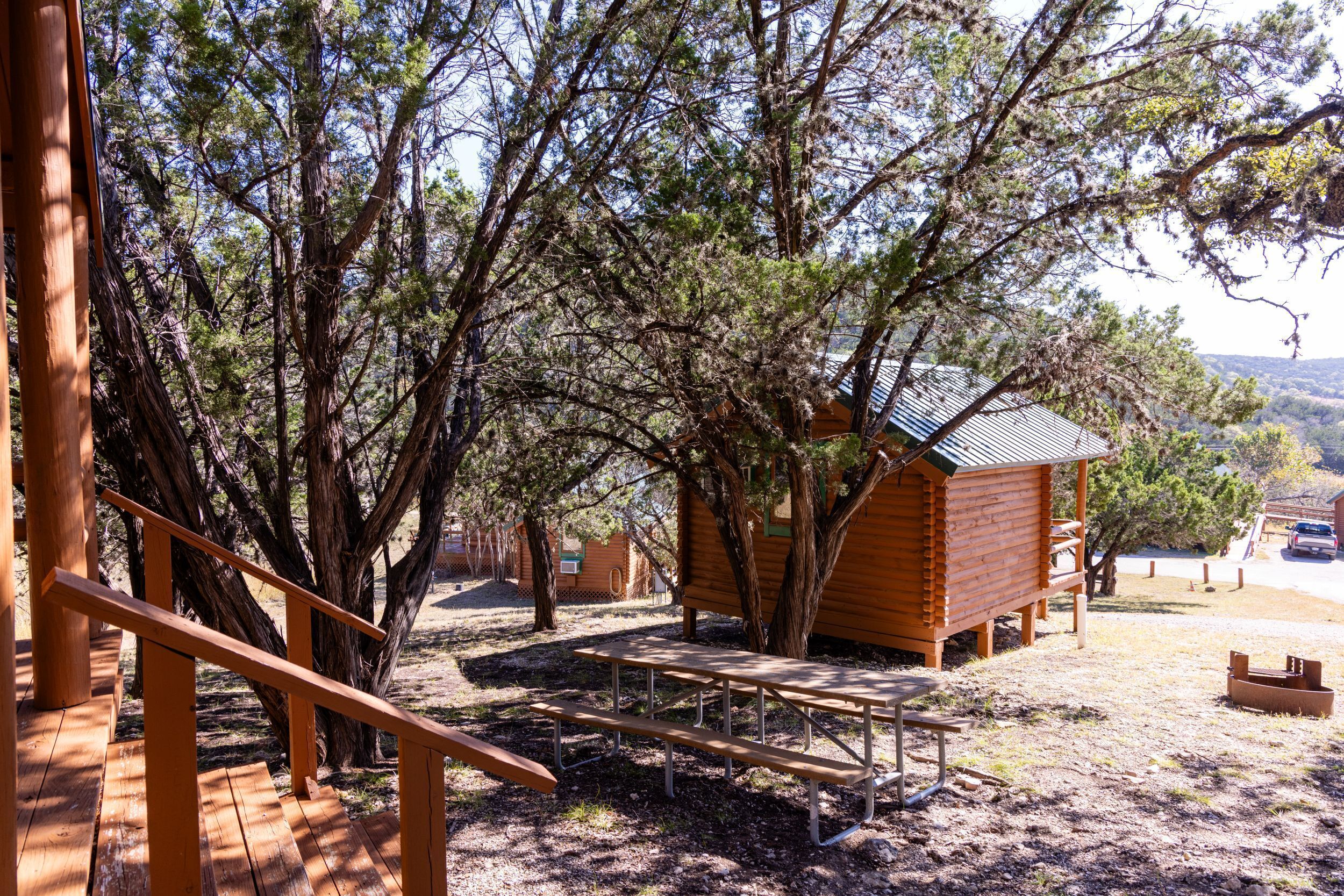 Una cabaña de madera con una mesa de picnic y una escalera que lleva a ella, rodeada de árboles.