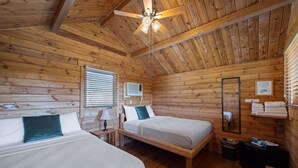 Habitación tipo cabaña de madera con dos camas, un ventilador de techo, un espejo y un estante con toallas.