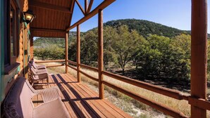 Una terraza de madera con sillas de mimbre, barandilla de madera y vista a un paisaje boscoso.