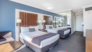 A hotel room with two beds, a sofa, a round table, and a mirror.