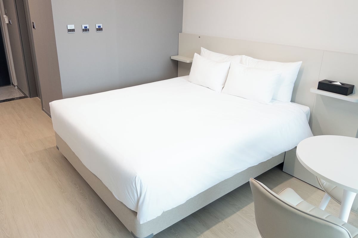 A modern hotel room with a large bed, bedside tables, a small round table, and a door.