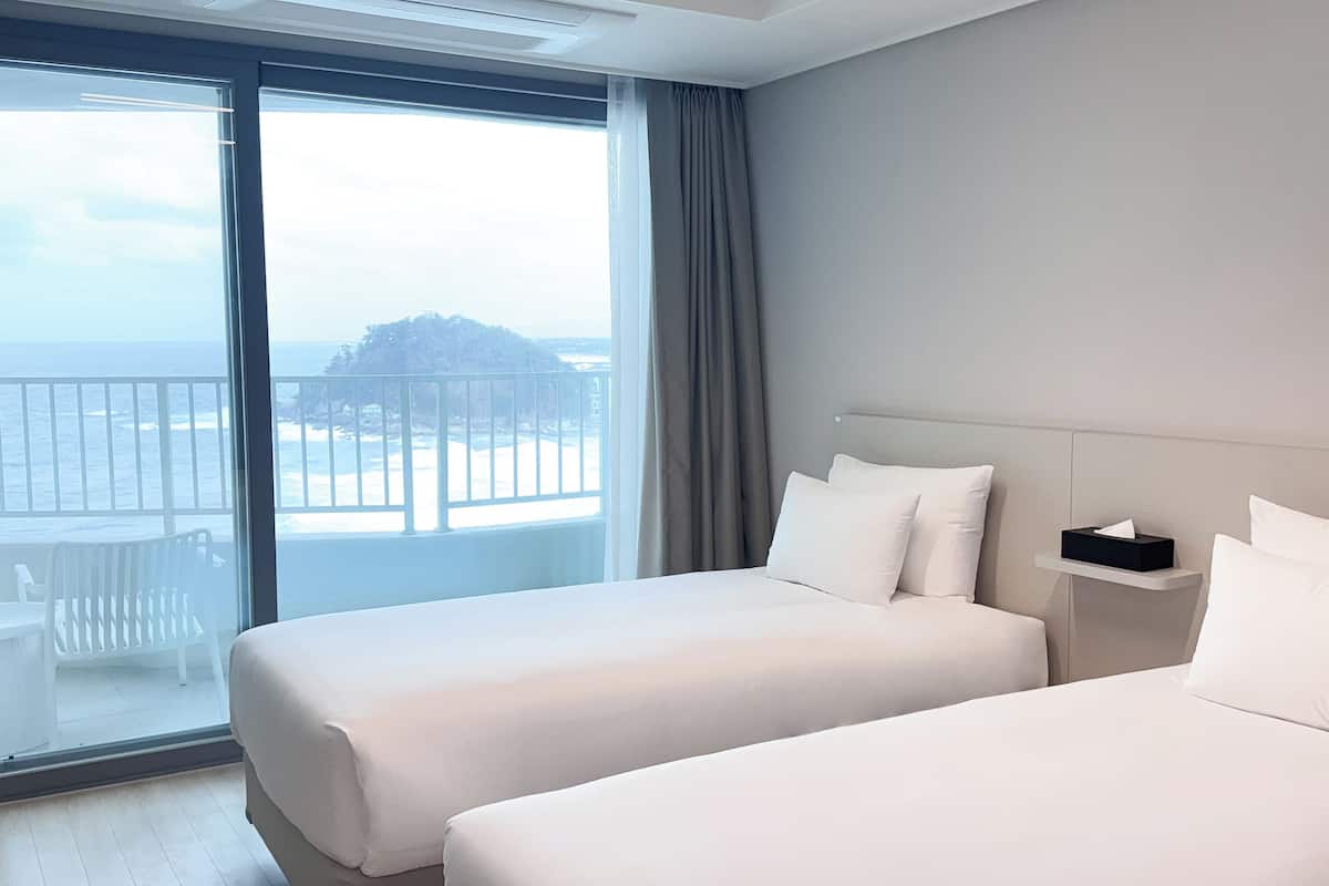 A hotel room with two beds, a balcony with a view of the sea, and a small table with a tissue box.