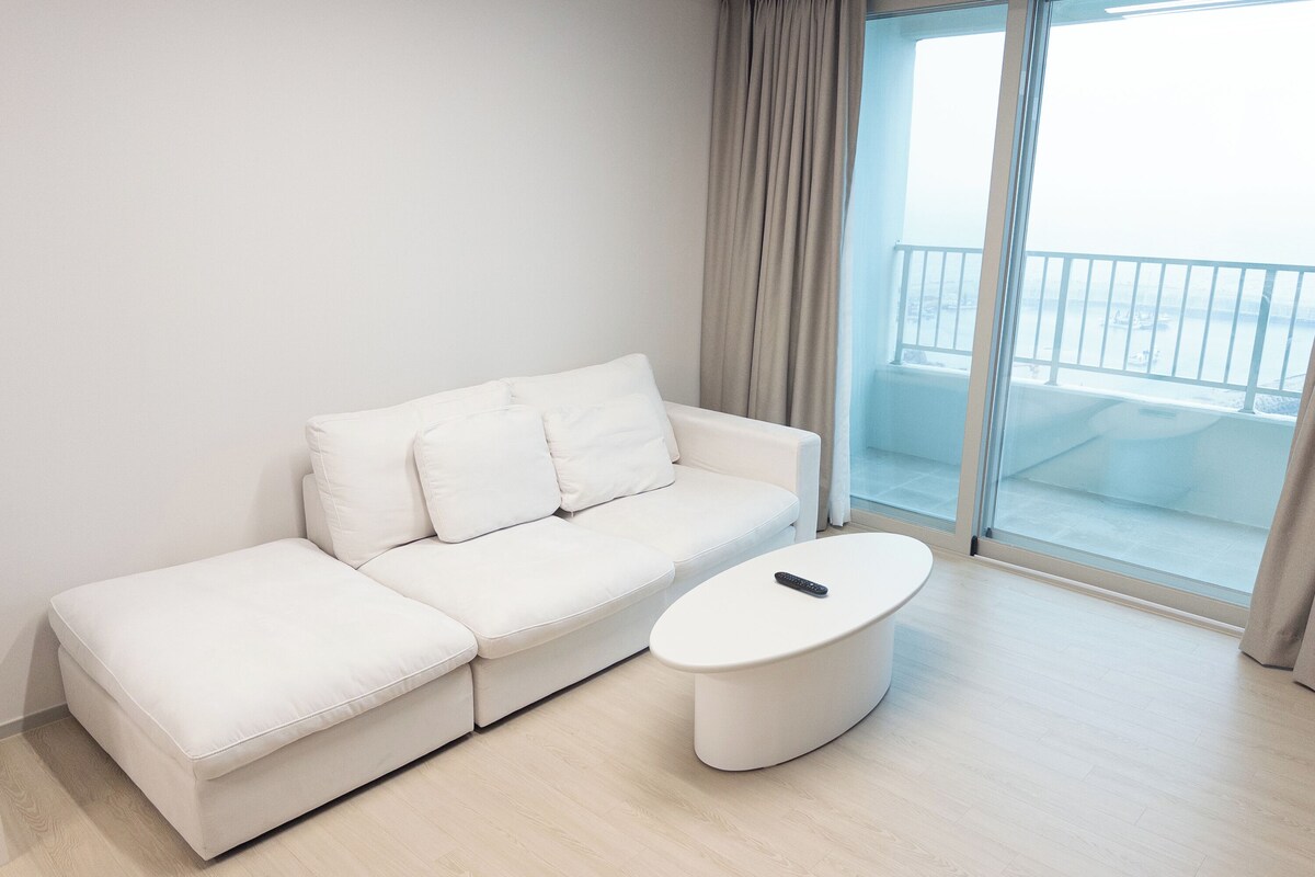A modern living room with a white sofa, a round coffee table, and a view of the city through large windows.