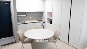 A compact kitchen with white cabinets, a round table, and beige chairs. - Hotel Wavellent Yangyang (Yangyang)