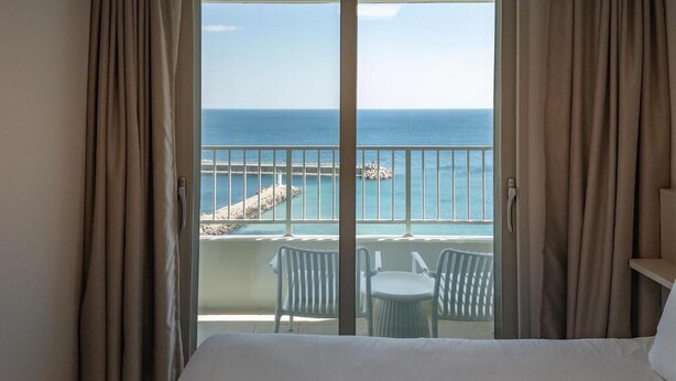 A hotel room with a balcony overlooking the sea, featuring a bed, two chairs, and a small table. - Hotel Wavellent Yangyang (Yangyang)