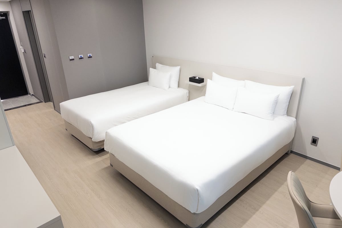 A hotel room with two beds, a bedside table, a chair, and a small table.