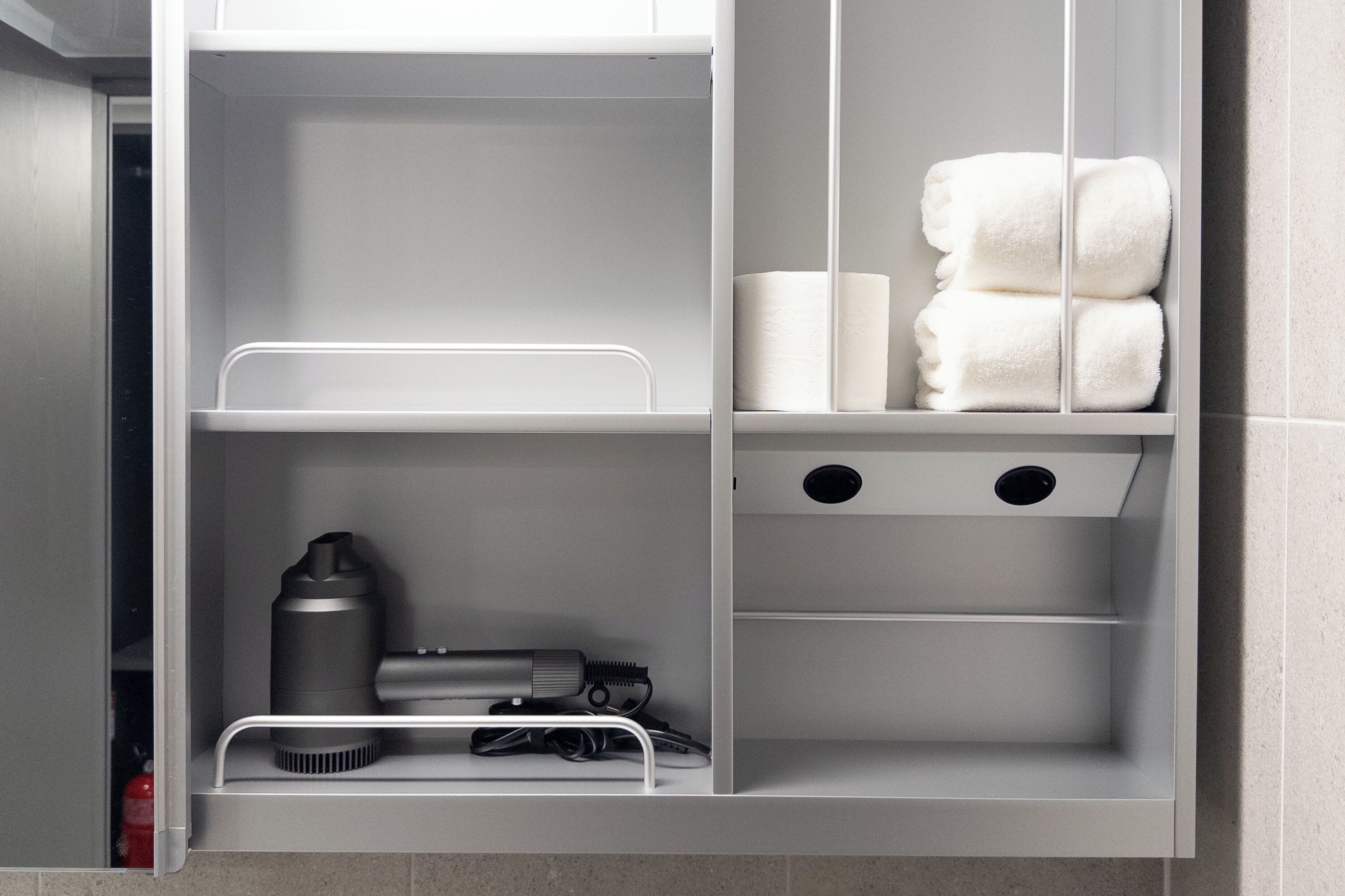 A bathroom with a white towel rack, a towel dispenser, and a shelf with a water bottle and a hairdryer.