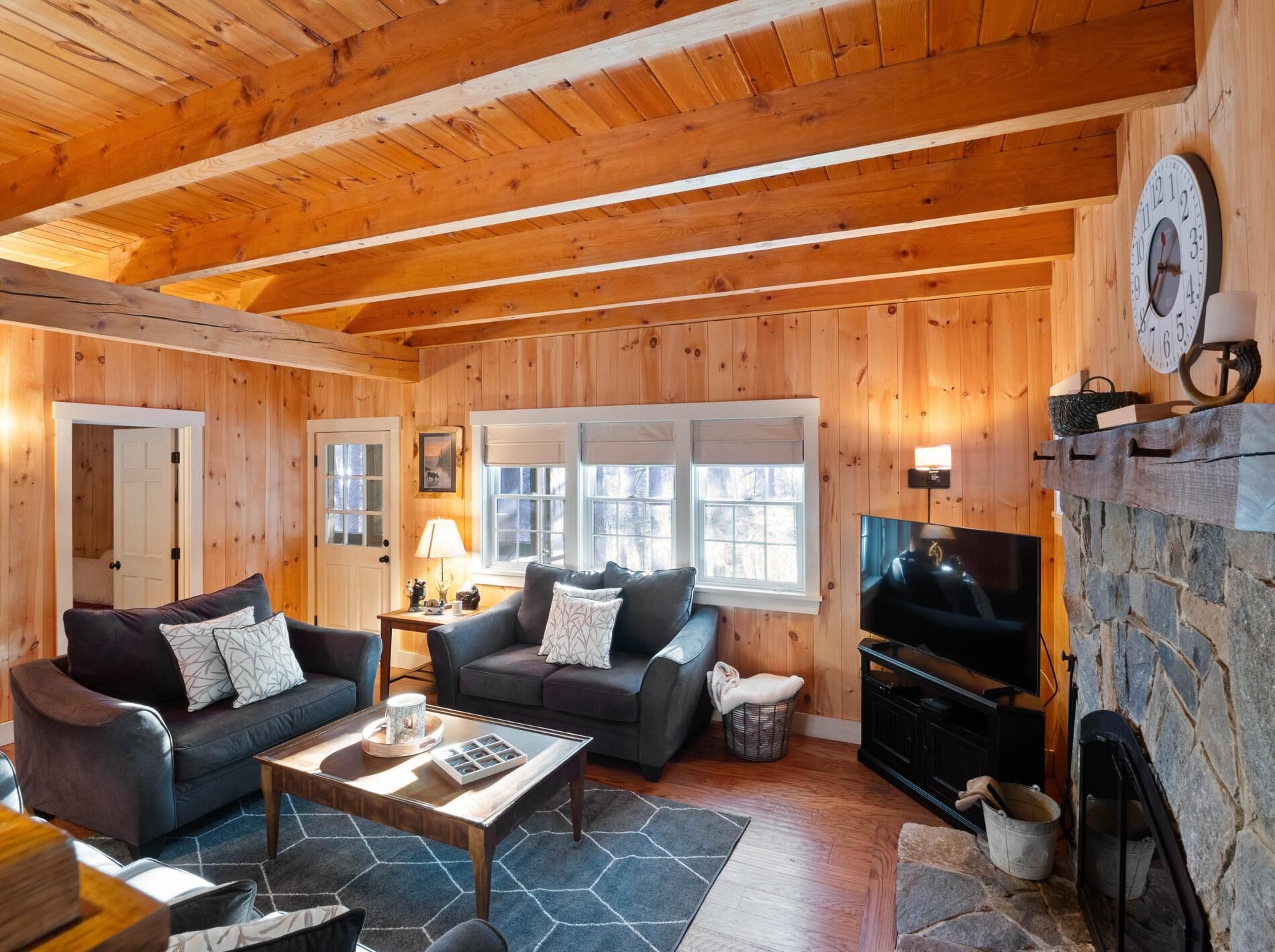 A cozy log cabin interior with two sofas, a coffee table, a fireplace, and a television.