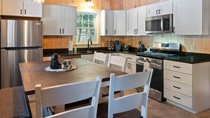 Une cuisine moderne avec des meubles blancs, des appareils en acier inoxydable et une table à manger en bois, assortie de chaises.