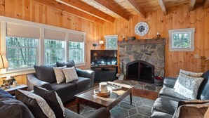 L’intérieur chaleureux d’un chalet en bois, avec une cheminée en pierre, des murs en bois et une grande fenêtre donnant sur une forêt.
