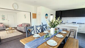 A modern kitchen with dark cabinets, a wooden dining table set for six, and a living area with a sofa and a coffee table. - Spacious 5BR 2BA plus sleepout & games room Family Home (Christchurch)