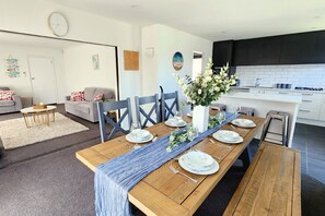A modern kitchen with dark cabinets, a wooden dining table set for six, and a living area with a sofa and a coffee table. - Spacious 5BR 2BA plus sleepout & games room Family Home (Christchurch)