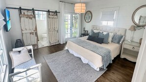 Un dormitorio con una cama grande, una mesita de noche, una silla, una alfombra, una lámpara colgante y una ventana con cortinas.