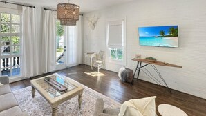 Una sala de estar con una mesa de centro de vidrio, un sofá, un televisor montado en la pared y un mueble de madera.