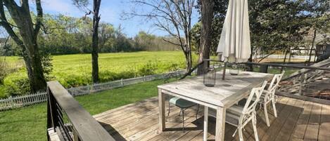 A wooden deck with a table and chairs, an umbrella, and a view of a green field.
