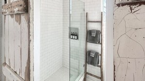 Un baño en esquina con paredes de azulejos blancos, cerramiento de ducha de vidrio y un perchero de madera.