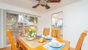 A dining area with a wooden table set for four, a ceiling fan, and a view of the outdoors through large sliding glass doors.